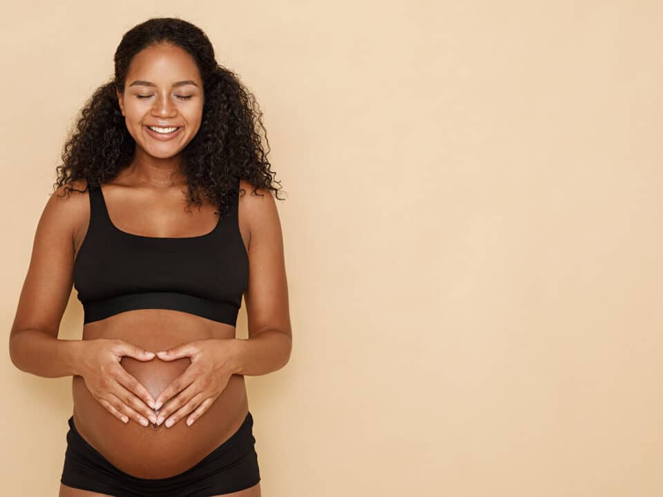 mulher grávida com as mãos na barriga, formando um coração